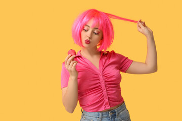 Beautiful young woman in pink wig with sweet macaroon on yellow background
