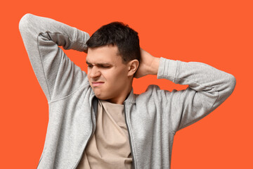 Handsome young man feeling bad smell from armpits on orange background