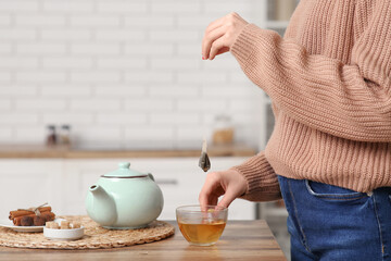 Young woman making tea with tea bag on table in kitchen