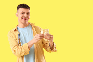 Handsome young man with tasty doner kebab on yellow background