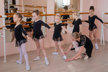 Fototapeta premium Children's ballet school. Caucasian woman teaching ballet to little girls. 