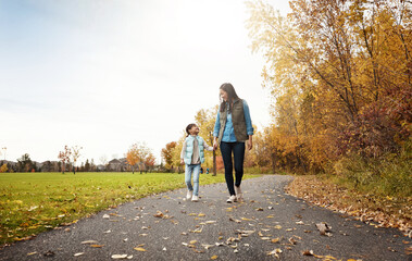 Mom, walking and holding hands with child for bonding, outdoor adventure or journey in nature. Happy mother strolling with daughter, kid or little girl on sidewalk in autumn season at park together