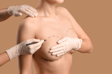 Plastic surgeon marking woman's breast on brown background, closeup