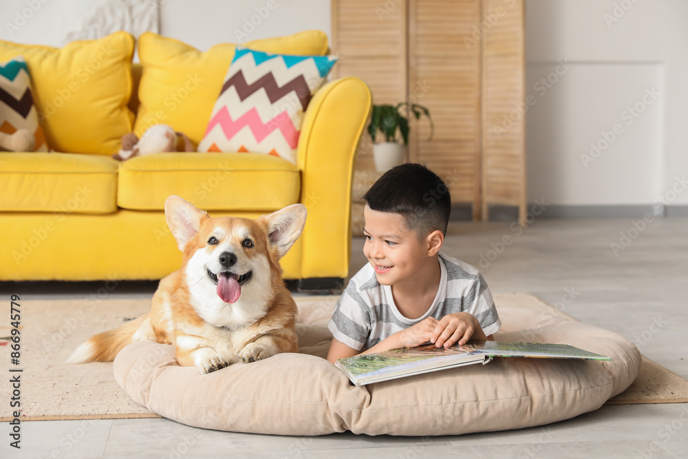 Wall mural Little happy Asian boy reading book with cute Corgi dog at home