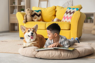 Little happy Asian boy reading book with cute Corgi dog at home