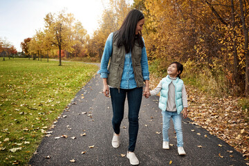 Fototapeta premium Walking, park and mother holding hands with girl for adventure, wellness and fresh air outdoors. Family, weekend and happy mom with young child on path for bonding, fun and relax together in nature