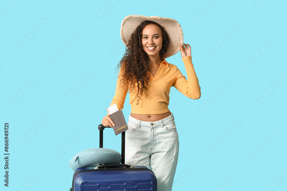 Poster happy young african-american woman with suitcase, passport and travel pillow on blue background