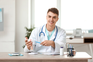 Young male doctor with spine model sitting at table in clinic