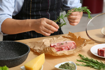 Young man with rosemary cooking meat at table in kitchen, closeup