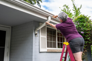 Middle aged white woman on a fiberglass ladder using a screwdriver to put together a rain gutter downspout after cleaning it out, homeowner maintenance  © knelson20