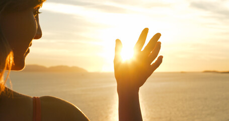 Fototapeta premium CLOSE UP, LENS FLARE: Female hand waves at golden setting sun over Adriatic Sea