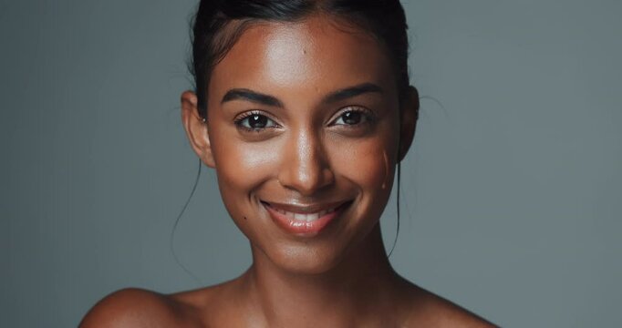 Face, skincare and Indian woman with natural serum for collagen in studio isolated on gray background. Portrait, smile and model apply dropper for cosmetics, dermatology and vitamin c for beauty