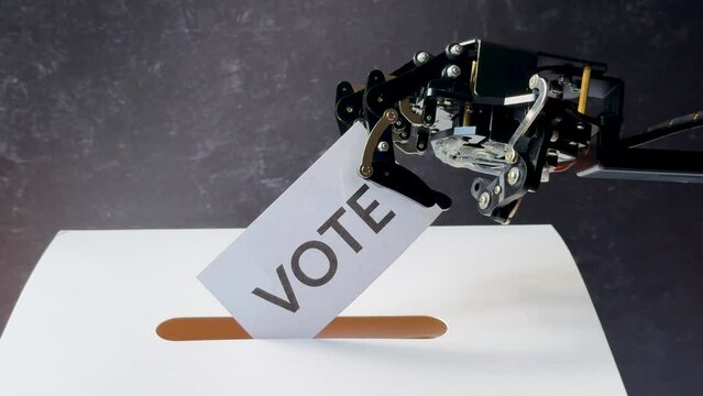 A robotic arm inserts a "Vote" card into a slot on a white surface with a dark background.