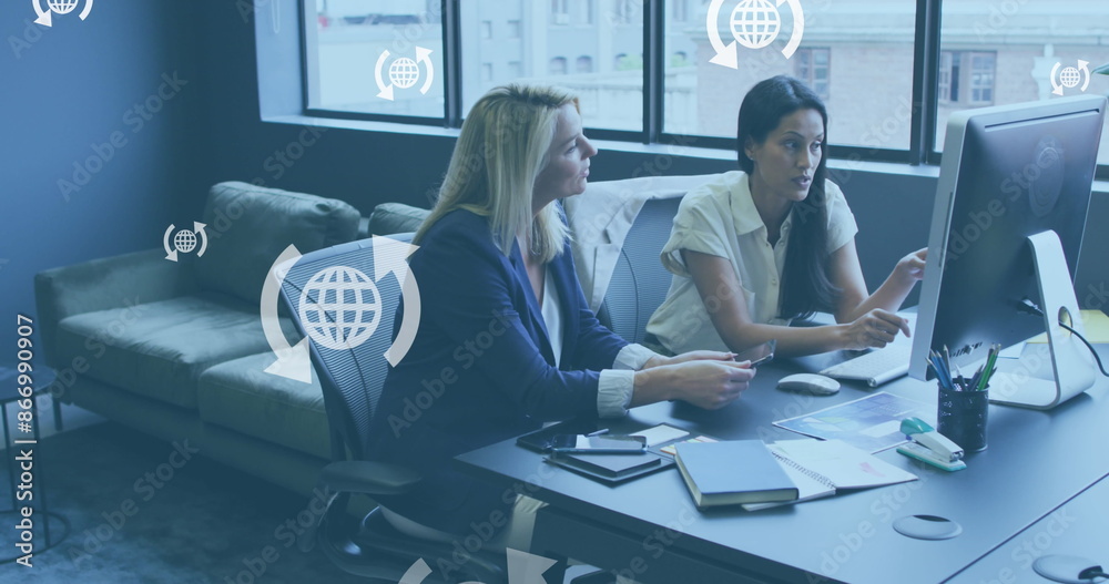 Wall mural Image of globe icons in arrows over diverse female coworkers discussing reports on computer