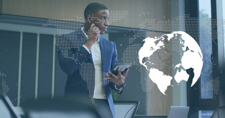 Image of spinning globe and world map over african american businessman using digital tablet