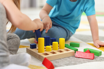 Little children playing with set of wooden geometric figures on carpet, closeup. Kindergarten activities for motor skills development