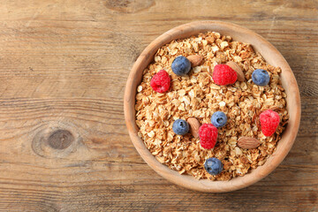 Tasty granola with fresh berries and nuts on wooden table, top view. Space for text