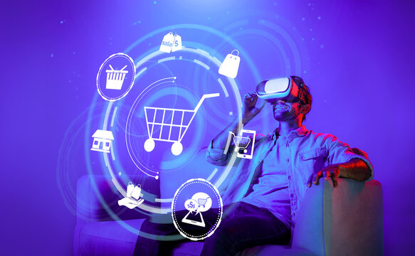 Happy man using VR headset and shopping online while sitting at sofa with shopping bags. Smart person looking at online market hologram and icon with neon background. Innovation technology. Deviation.