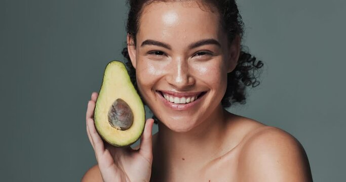 Woman, avocado and studio background with smile for beauty or skincare, repair or healing with vitamin e. Female person, backdrop and face with natural cosmetics, fruit oil for acne treatment