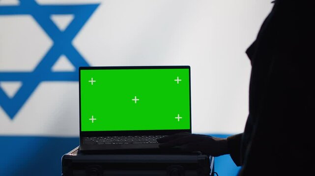 Israel secret police agent uses mass propaganda tools on green screen laptop to influence population minds and spread misinformation. Mossad spy commits PsyOp sabotage using mockup notebook, camera A