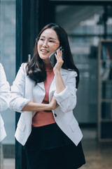 Fototapeta premium Portrait of a happy Asian businesswoman using mobile phone indoor, Asian businesswoman working in modern office.