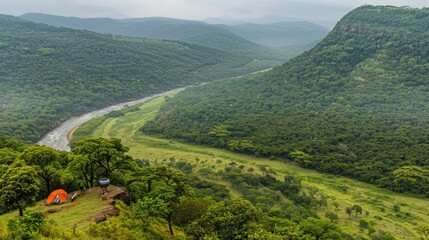A scenic campsite on a hilltop overlooking a lush, green valley with a river winding through it and a forested mountain range in the background.