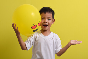 Emoticon in love. Cute Asian boy holding romantic love face emoticon balloon isolated on yellow background