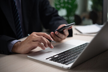 Hands of businessman using smartphone and laptop, indicating modern business communication and multitasking. Perfect for corporate environments, tech firms, productivity themes. 