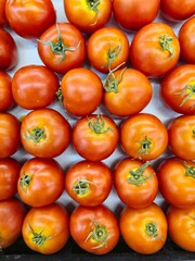 Background of tomatoes at a market, featuring fresh, ripe, red tomatoes with green stems, showcasing their vibrant color and organic, healthy appearance