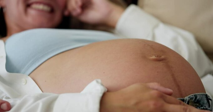 Close up of happy brunette pregnant woman laughing big belly of pregnant woman stroking with hand at home