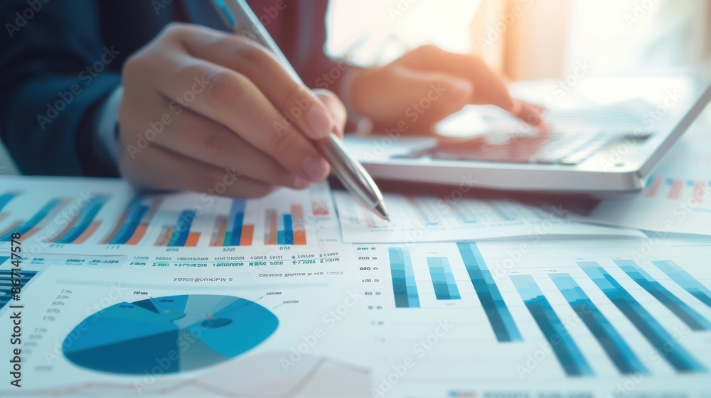 Poster close-up of businessperson analyzing financial graphs and charts with a pen and laptop in a modern o