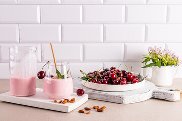 Delicious summer dessert cherry smoothie in a large glass glass with eco straw and a dish with washed ripe cherries by a white brick wall