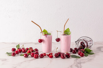 Two chic glasses with a delicate chilled smoothie or a cocktail with metal straw on a marble table among the numerous ripe cherries. Front view.