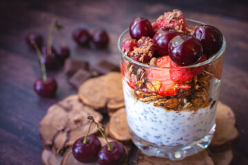 Chia pudding with strawberries, cherries, granola, and chocolate on a wooden desk.