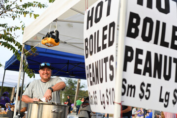 Smiling vendor selling hot boiled peanuts at an outdoor market.