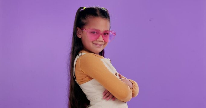 Sunglasses, crossed arms and face of child in studio ready for summer vacation, adventure or holiday. Smile, portrait and girl kid with heart shape accessory for weekend trip by purple background.