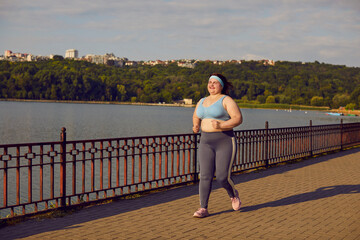 Portrait of a fat overweight happy woman running across the bridge in the city summer park. Plump...