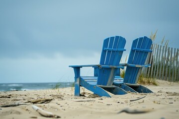 Two blue wooden chairs standing on a sandy beach, overlooking a tranquil ocean view