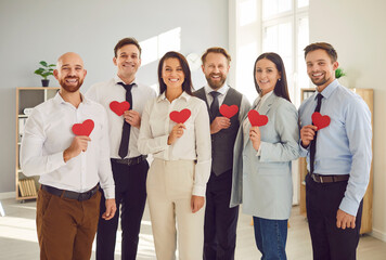 Portrait of a diverse group of happy businesspeople stands in the office, holding red hearts and...