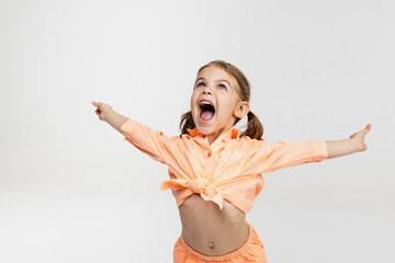 Portrait of a surprised little girl on a white background. Looking at the camera. screams, shows bright emotions Raises his hands up. Advertising of children's products