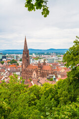 Germany, Freiburg im Breisgau aerial panorama view above old town houses, marketplace, red roofs and historical muenster cathedral building behind green tree tops