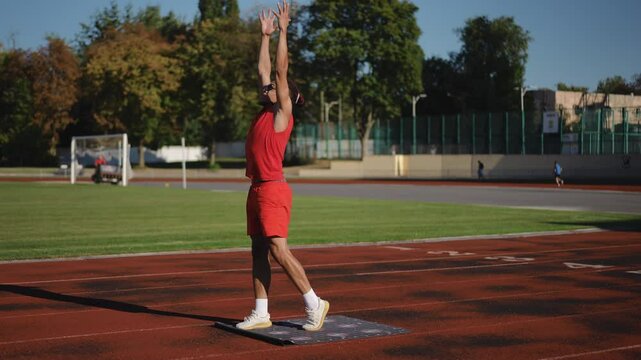 Male athlete during training on the platform P9. A man performs exercises while standing on a fitness mat for 3D training on a stadium running track on an autumn day