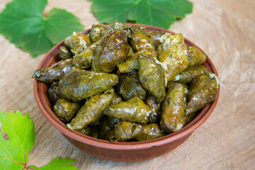 Dolma a stuffed grape leaves in a clay bowl on wooden background