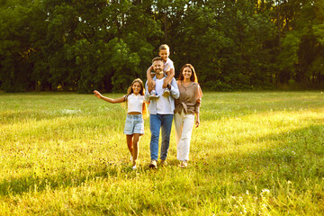 Fototapeta premium Portrait of happy smiling family with son and daughter standing in the summer park and looking cheerful at camera. Mother, father with two kids walking in nature enjoying sunny day together.