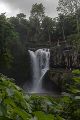 Obraz premium Cascading multi-level waterfall named Tegenungan Waterfall in the middle of a rainforest. Thin water flows rush down and form a reservoir. Dense dark jungle and tropical greenery around.