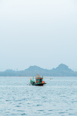 A small fishing boat that fishermen take out to catch fish during the day, with a beautiful mountain range in the background at Koh Phithak, Thailand.