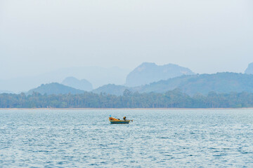 A small fishing boat that fishermen take out to catch fish during the day, with a beautiful mountain range in the background at Koh Phithak, Thailand.