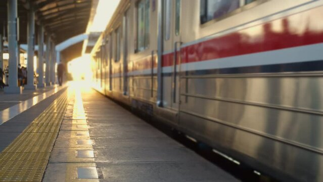 A commuterline electric train car is running in the morning with many passengers waiting by the rail, yellowish sunlight in the distance