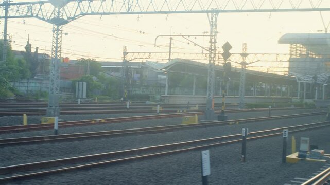 A commuterline electric train pulls into the station, a view taken from inside the window of the train car in the morning with yellowish sunlight.
