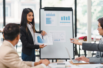 Naklejka premium Smiling businesswoman presenting charts and graphs on whiteboard during meeting in modern office.